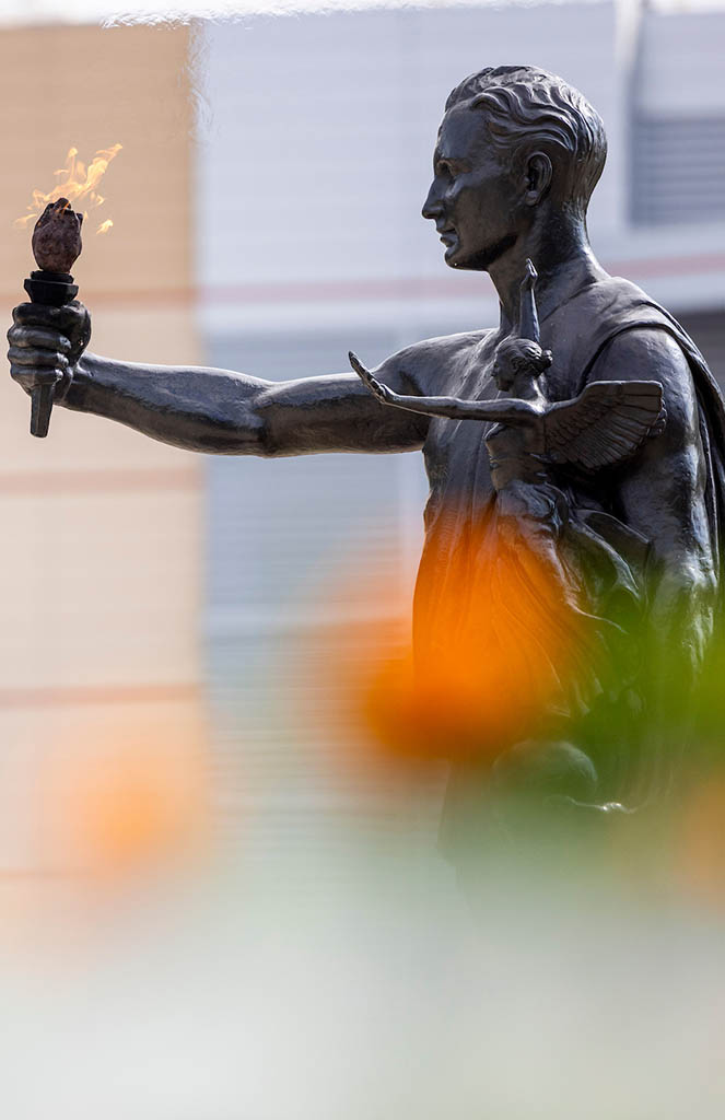 A photo of the torchbearer statue behind marigold flowers. Photo by Craig Bisacre / University of Tennessee.